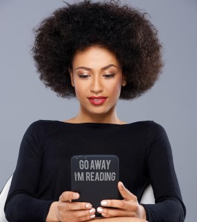 A black woman reading an ereader. The ereader has a signs saying "go away. I'm reading"